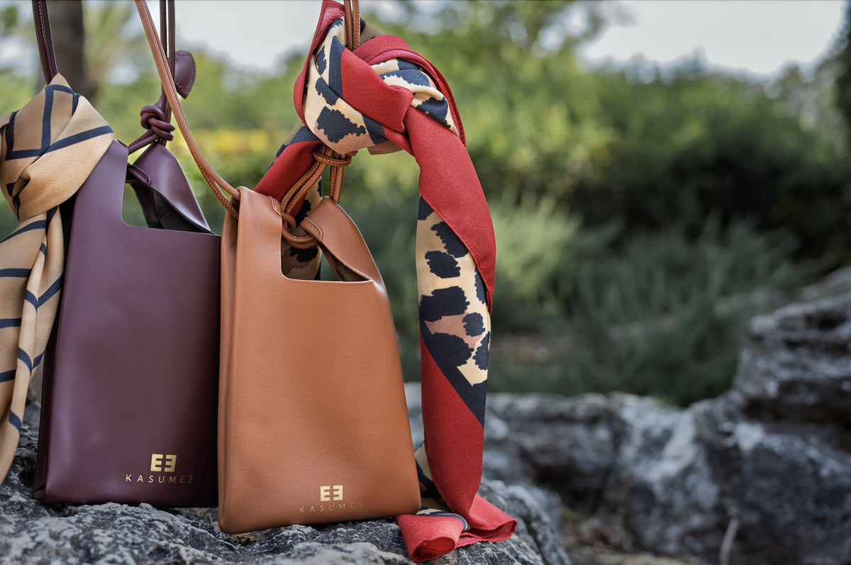 Burgundy and caramel KASUMEE leather crossbody phone bags styled with silk scarves on a stone
